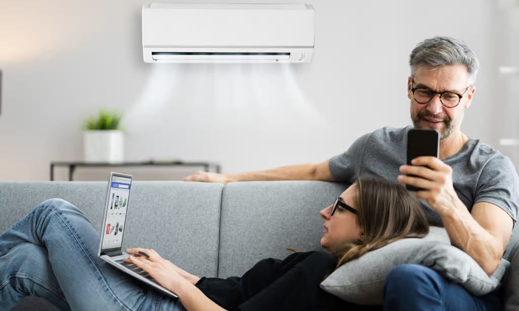 a man and woman sitting on a couch with a laptop and a air conditioner