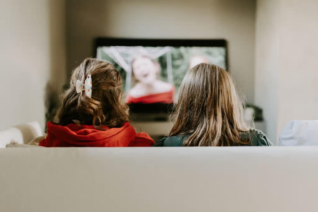 two girls sitting on a couch watching a television