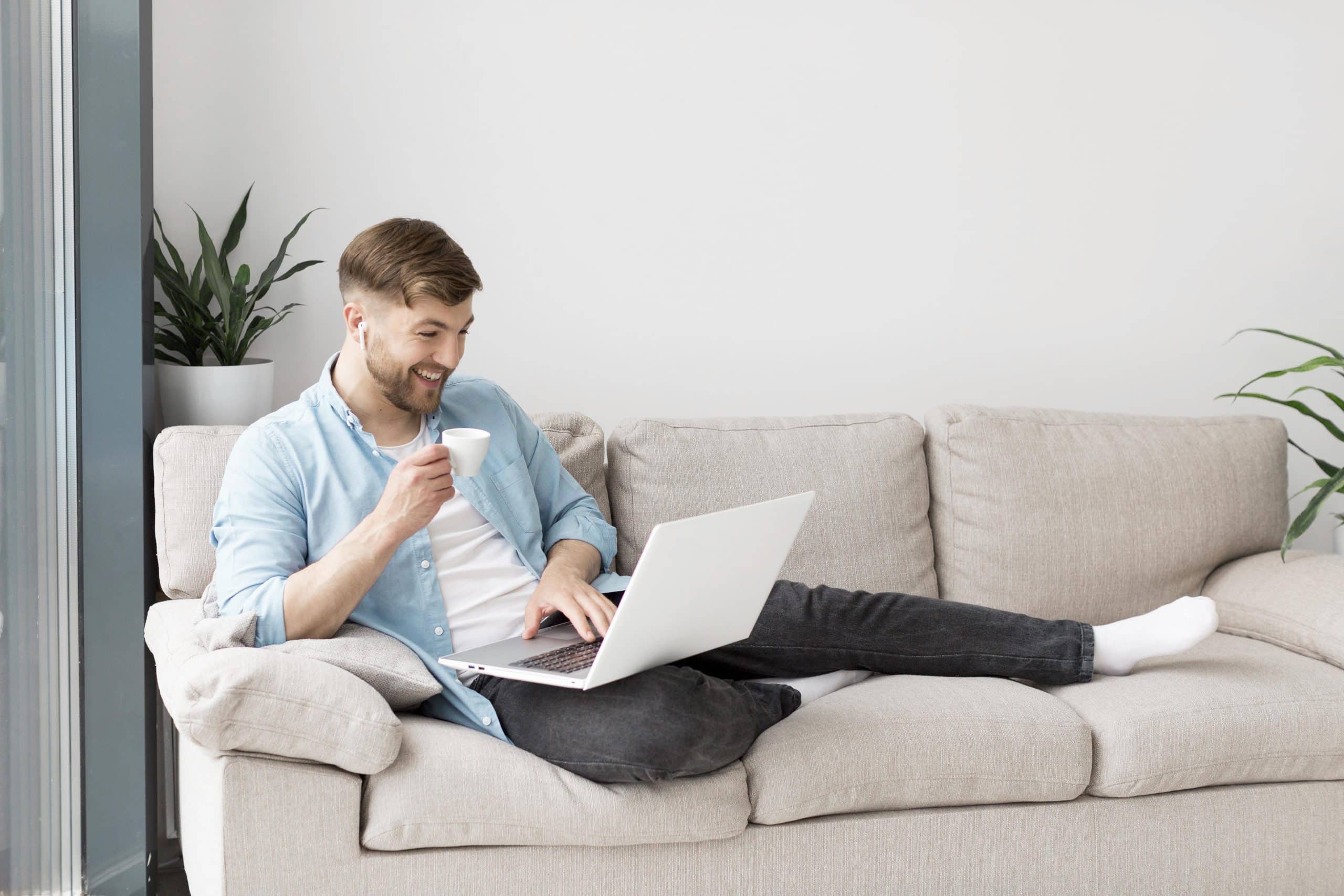 a man sitting on a couch with a laptop and a cup of coffee