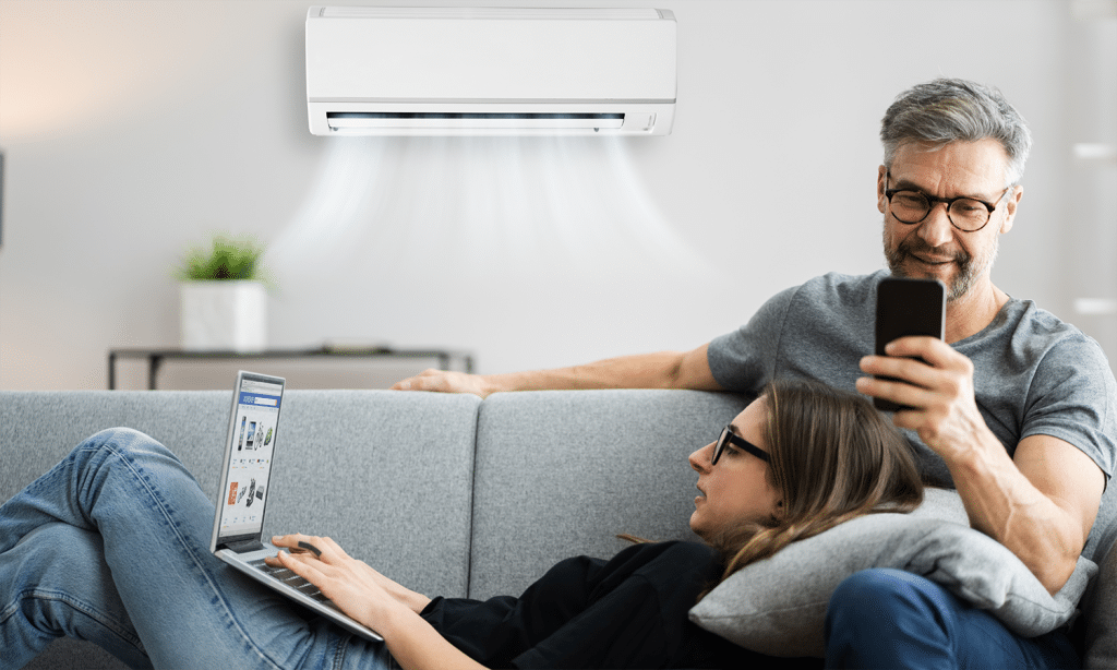 a man and woman sitting on a couch with a laptop and a air conditioner above them