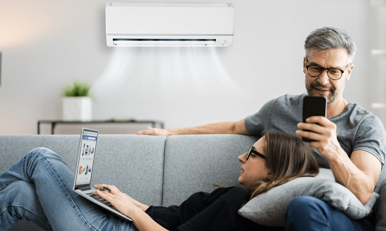 a man and woman sitting on a couch with a laptop and a air conditioner above them
